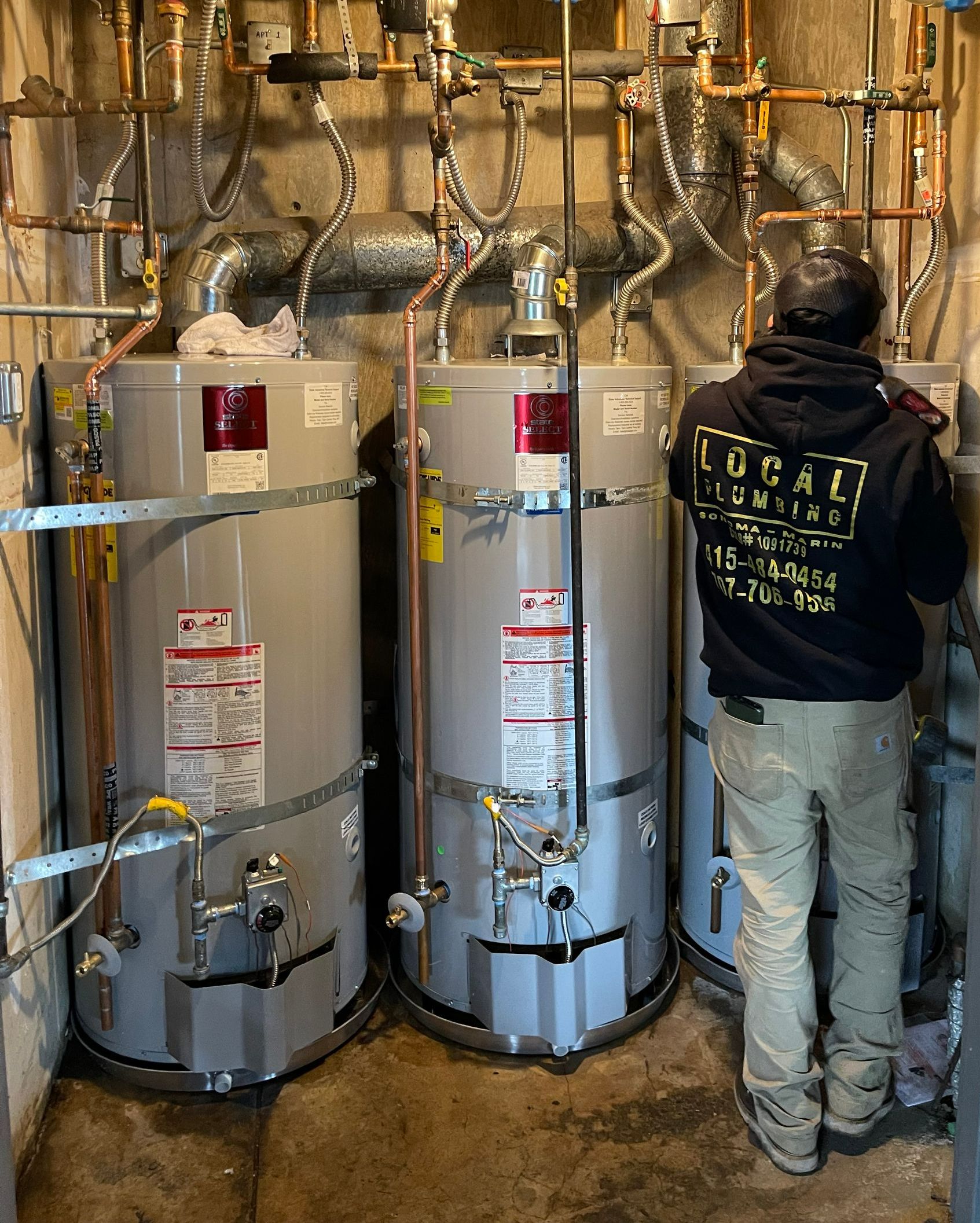 Three water heaters installed, with a worker inspecting the one on the right.