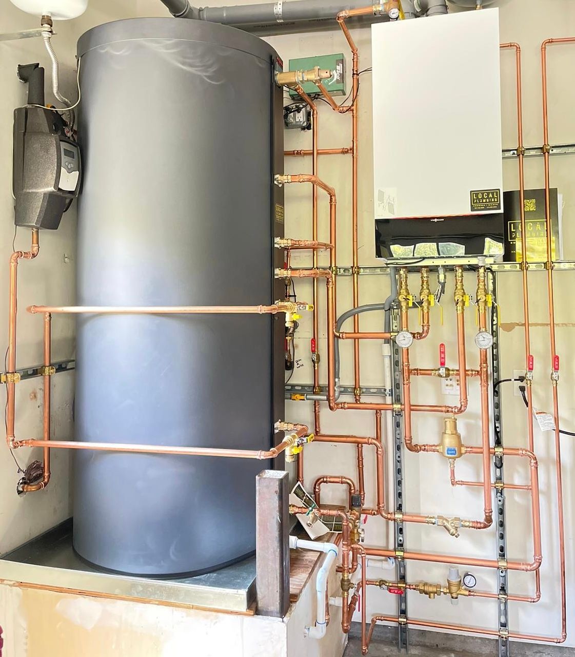 Copper pipes connected to a gray water heater and white wall-mounted boiler in a utility room.