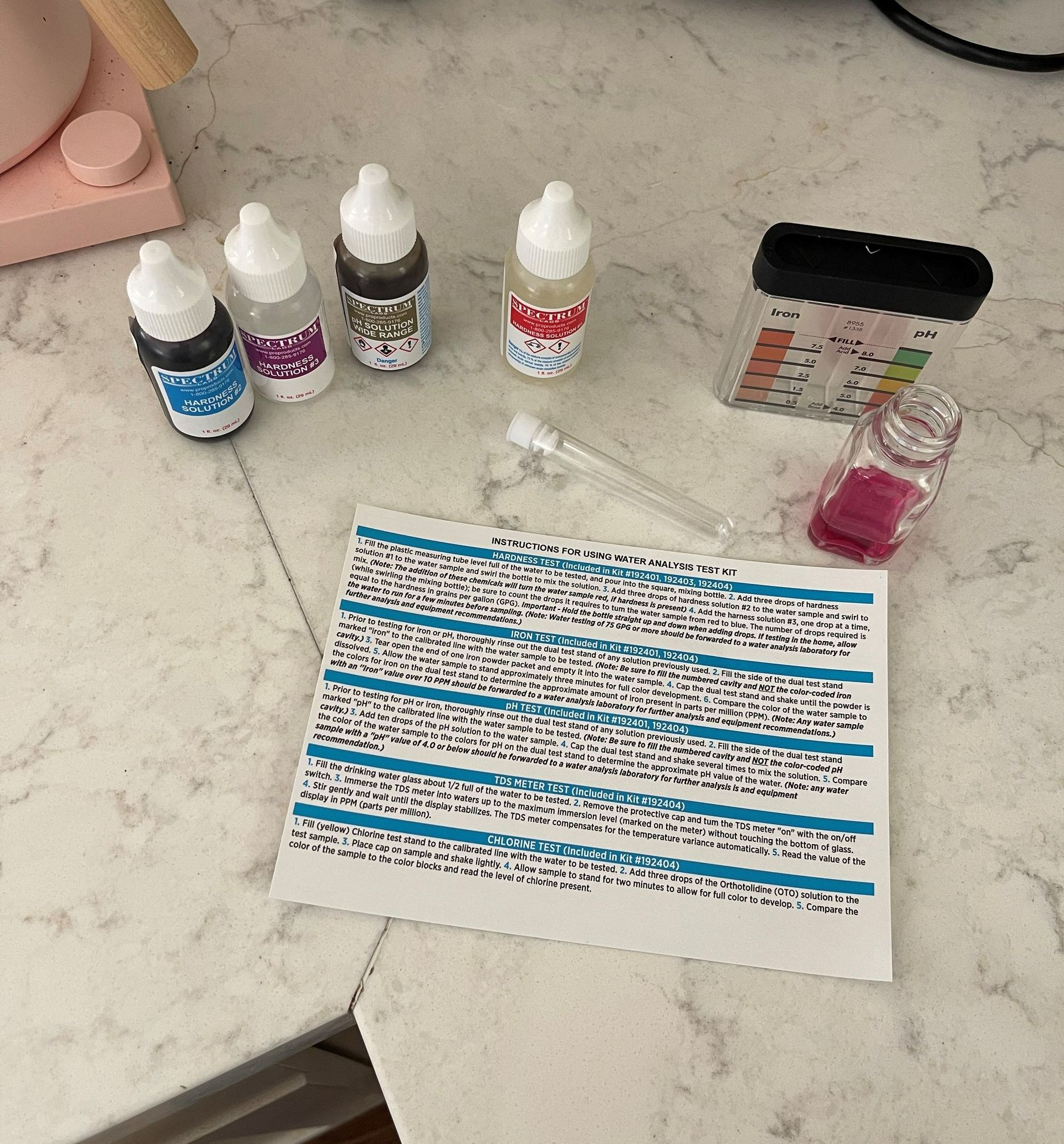 Water testing kit with bottles, vial, instructions, and color chart, on a table.