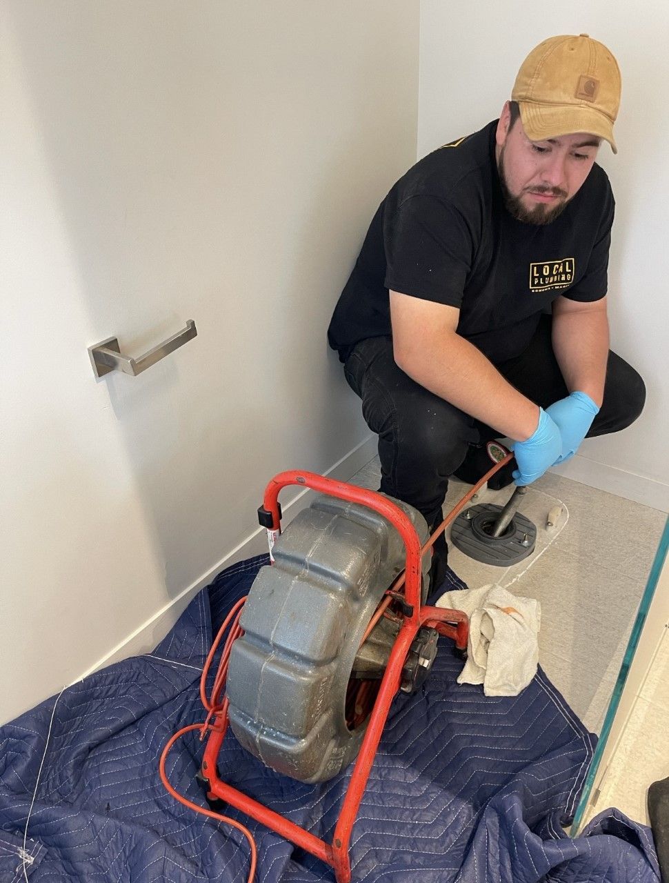 Plumber using drain inspection camera. Person in black shirt, blue gloves, and tan cap in a bathroom.