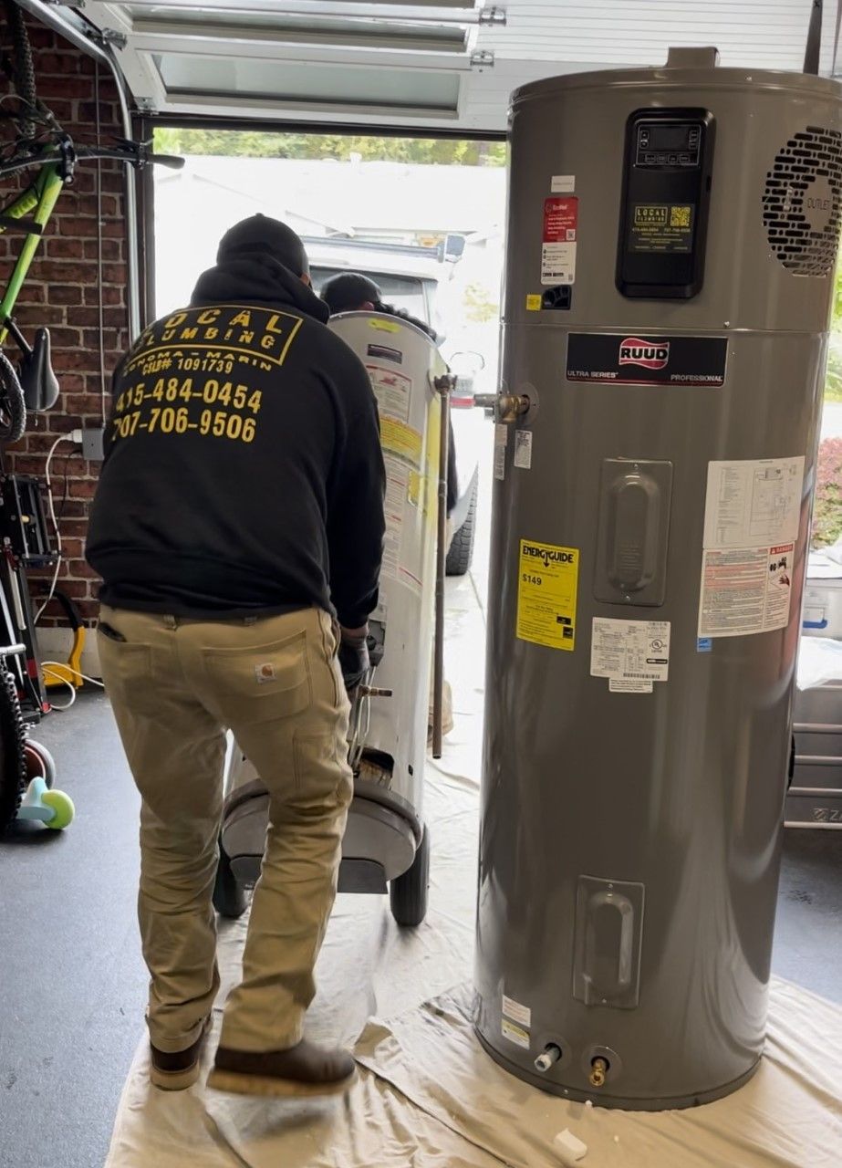 Two men moving a new water heater into a garage. The old heater is nearby.