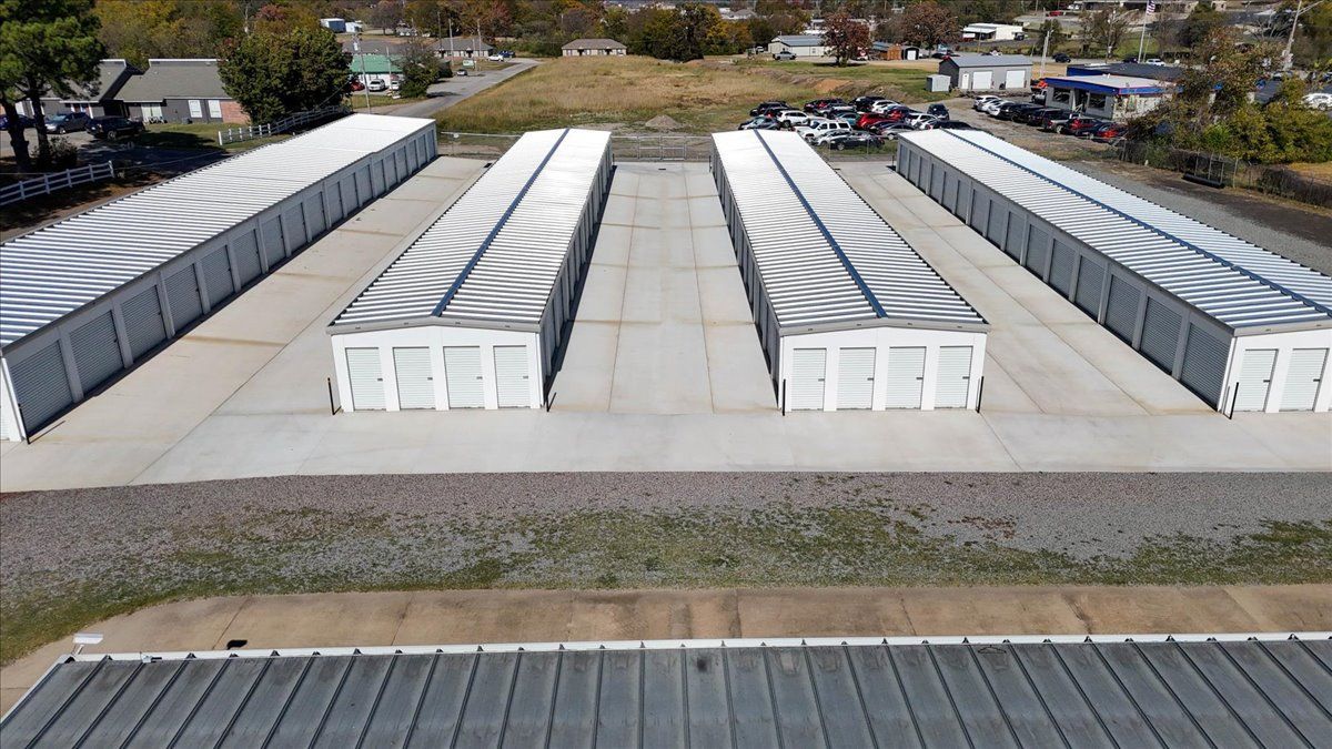Storage units lined up, outdoors. White units with concrete ground, green grass, and small buildings.
