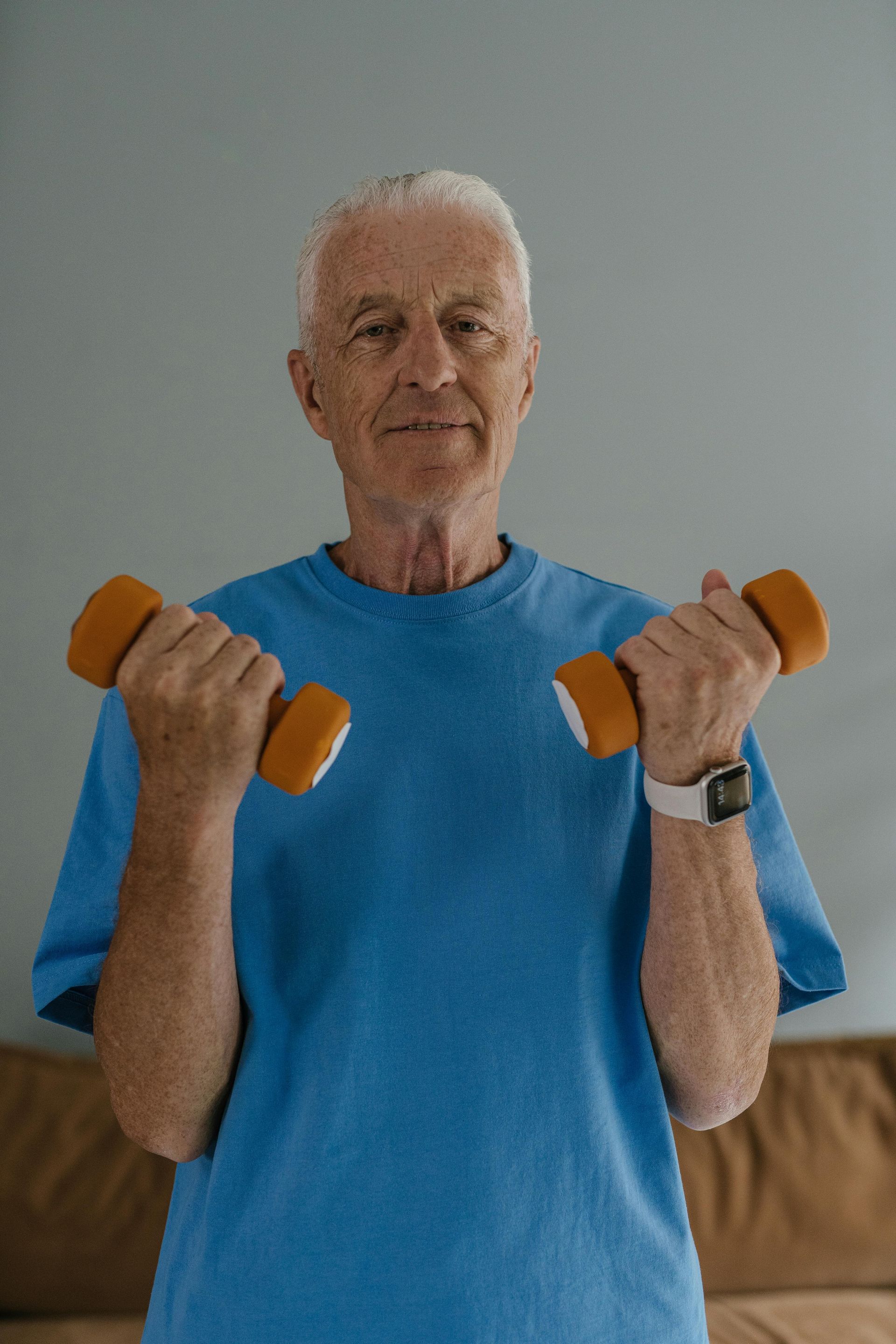 A person wearing a blue t-shirt performs bicep curls with two orange dumbbells in a room.