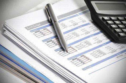 Una penna argentata e una calcolatrice nera sono appoggiate su una pila di fogli per la pianificazione del budget.