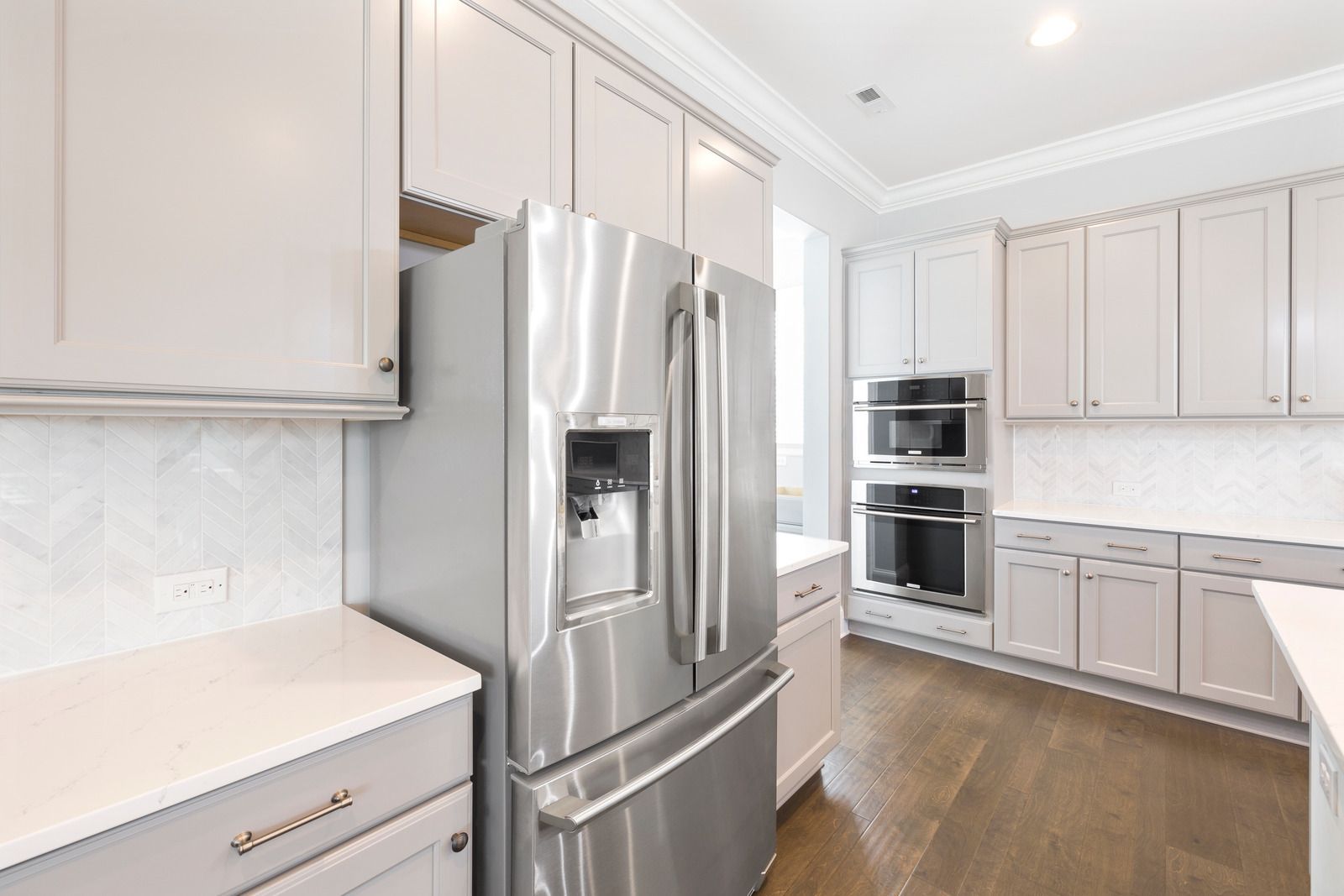 Stainless steel refrigerator in a bright kitchen with white cabinets and hardwood floors.