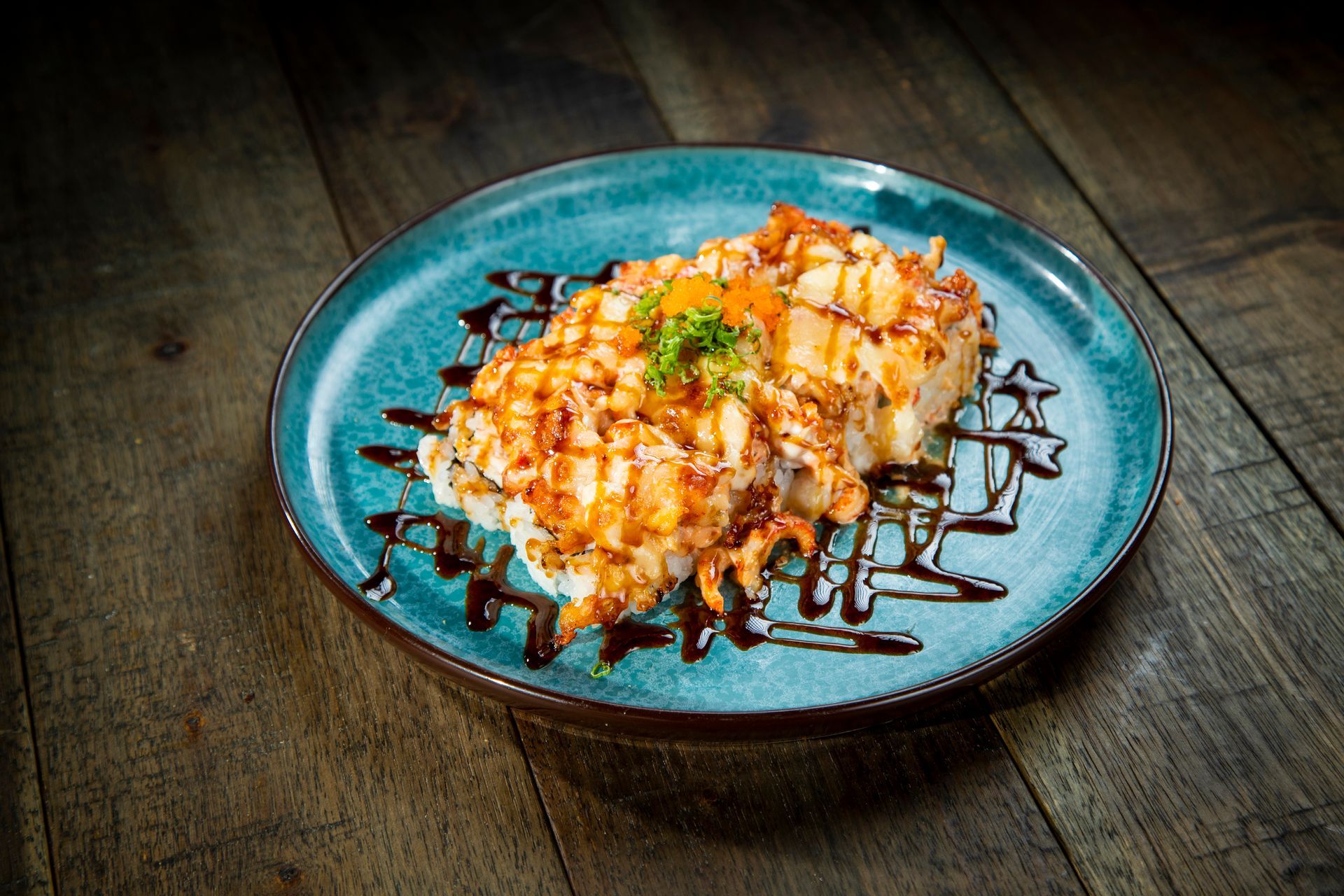 Cheesy baked dish on a blue plate, drizzled with dark sauce on a rustic wooden table