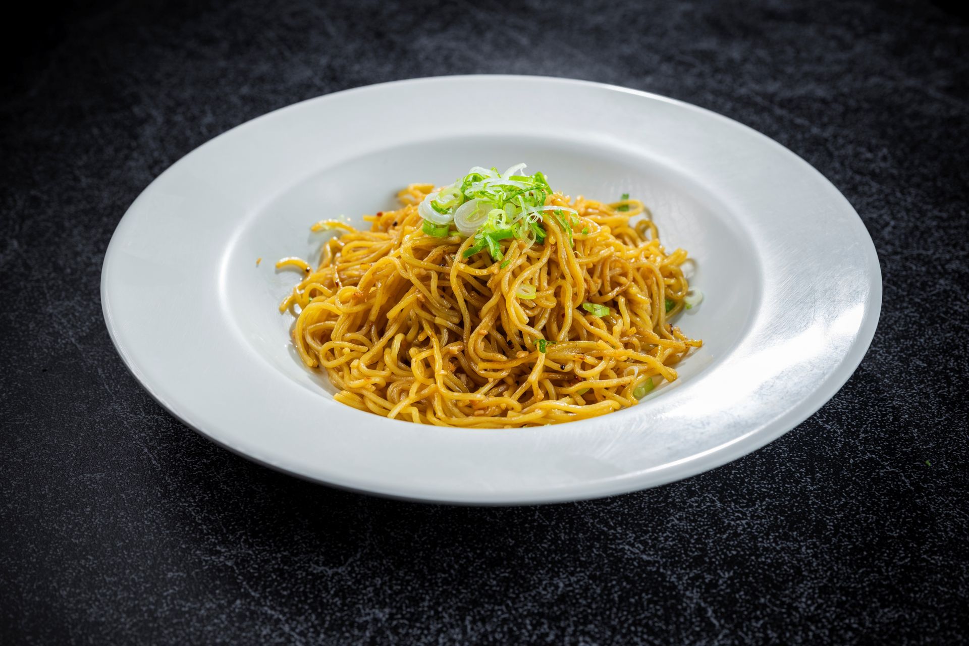 Plate of yellow noodles topped with herbs on a white dish against a dark background