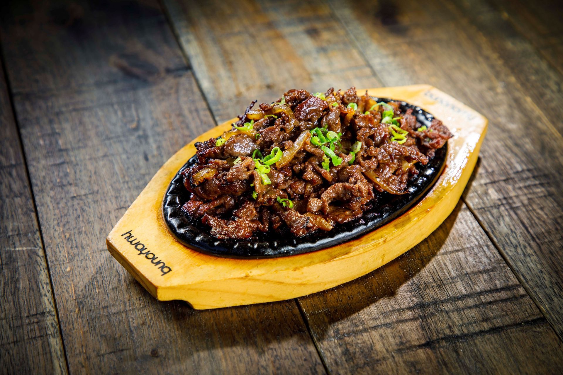 Sizzling grilled meat topped with herbs on a wooden serving platter on a rustic table