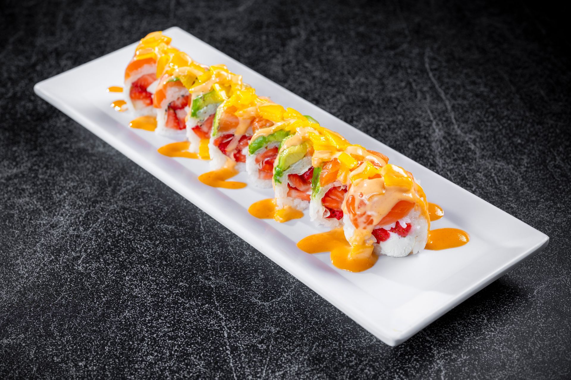 Sushi rolls drizzled with sauces on a white rectangular plate