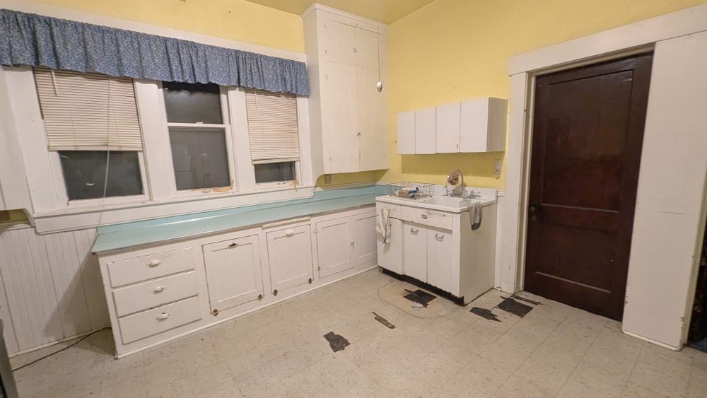 Kitchen with white cabinets, light blue countertops, and a dark wooden door.