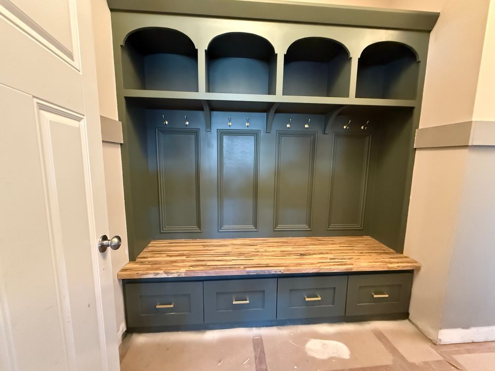 Green built-in mudroom with arch-topped cubbies, hooks, bench with drawers, and light wood countertop.