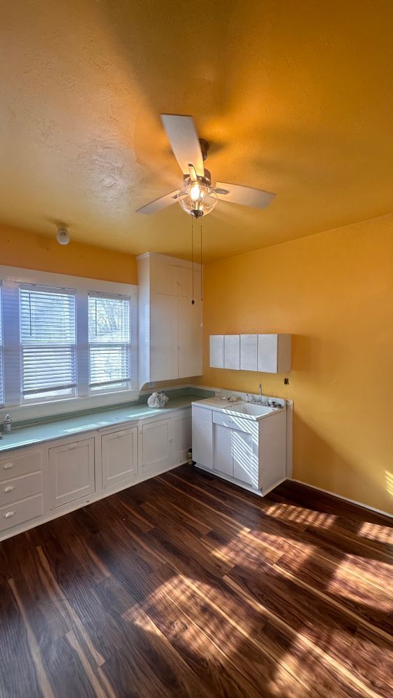 Yellow-walled kitchen with white cabinets, wooden floor, and a window seat with blinds.