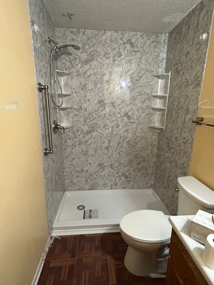 Shower stall with marbled gray walls, white shower base, toilet, and dark wood floor.