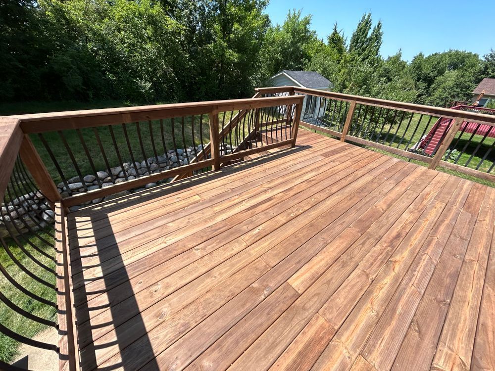 Wooden deck with dark railing, overlooking green grass and trees.