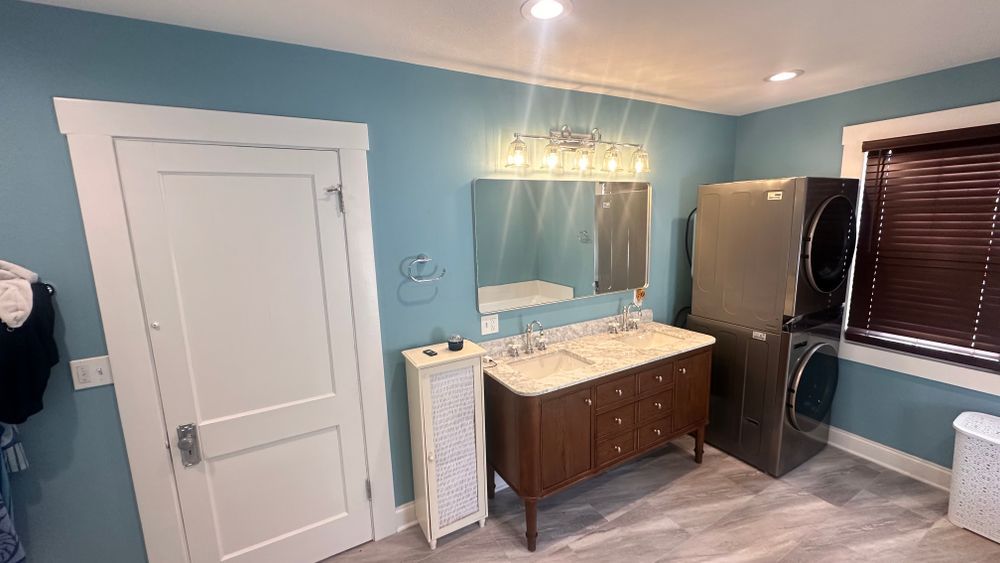 Bathroom with a double sink vanity, stacked washer/dryer, and blue walls.