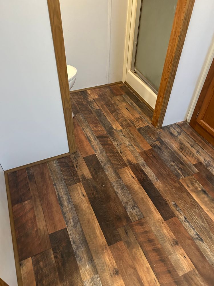 Wooden-look flooring in bathroom area with a white wall and shower visible.