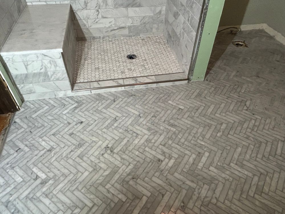 Herringbone marble tile floor leading to a marble shower with a bench seat.