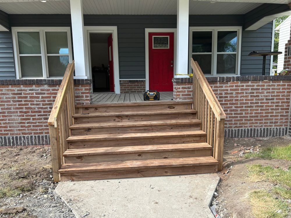 Wooden stairs leading to a house with a red door, windows, and brick and gray siding.