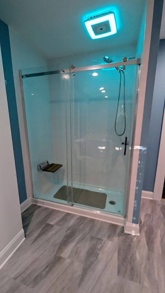 Modern bathroom with a glass shower, a bench, and gray flooring.