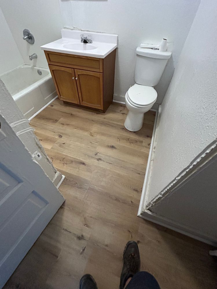 Bathroom with wooden floor, vanity, toilet, and tub. Light walls.