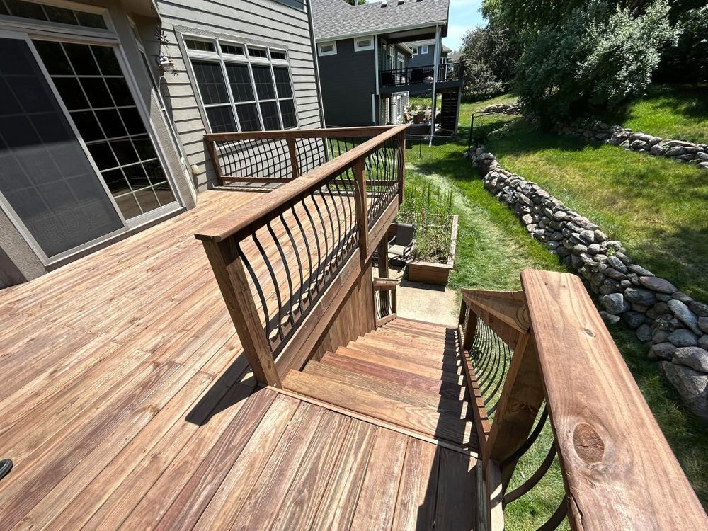 Wooden deck with stairs leading down to the backyard, iron railings, and lush greenery.