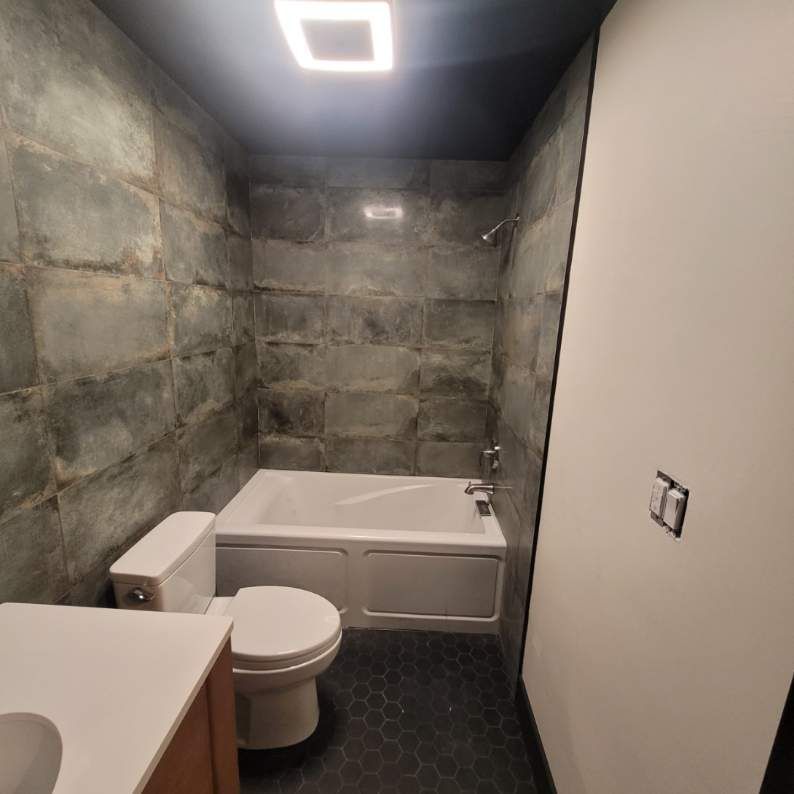Bathroom with a white tub, toilet, and sink. Gray stone tiles cover the walls.