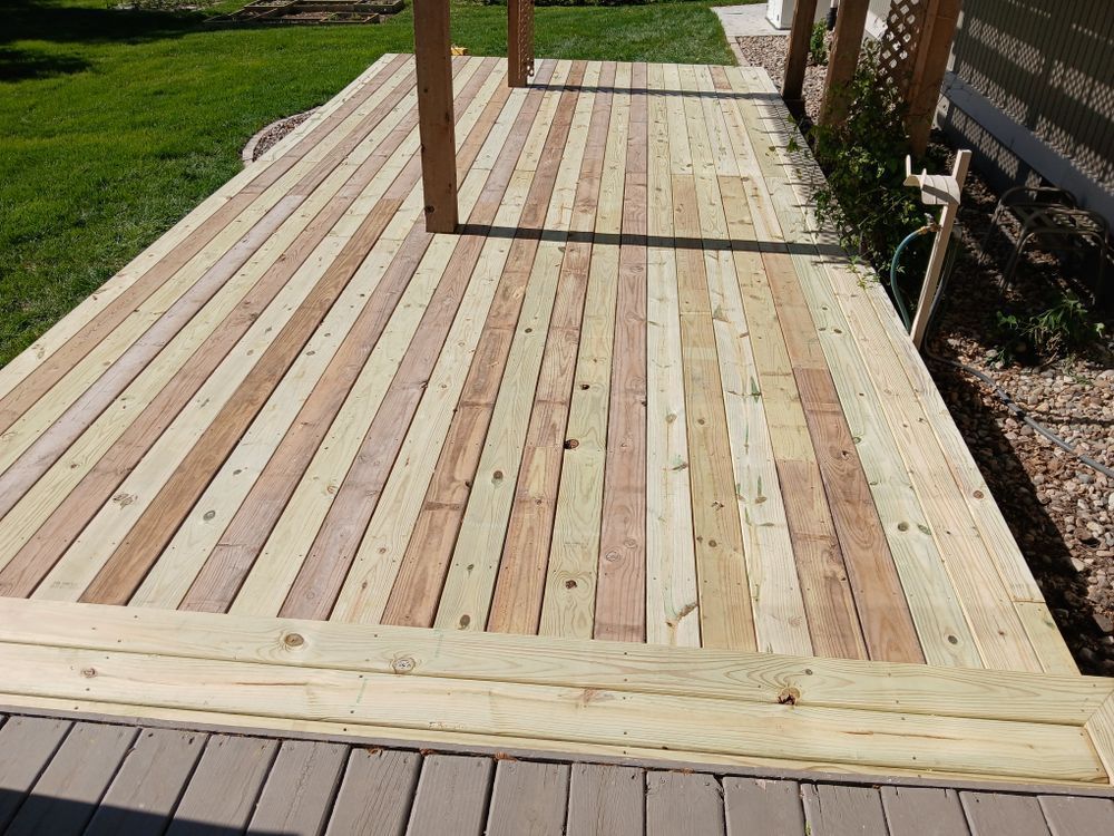 Wooden deck with light brown planks, surrounded by grass and a fence.