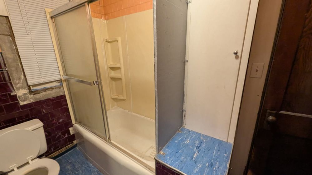 Bathroom with shower, toilet, and cabinet; blue flooring, pink and orange walls.