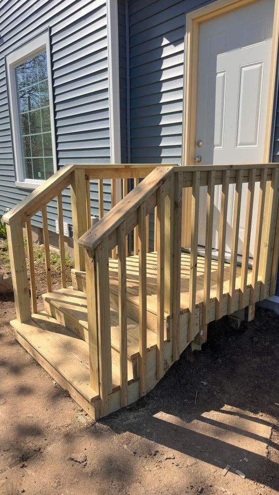 Wooden steps and handrails leading to a white door, set against a blue-sided building.