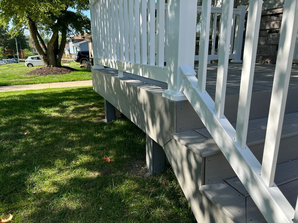 White railing on a composite deck with gray steps, beside green grass on a sunny day.