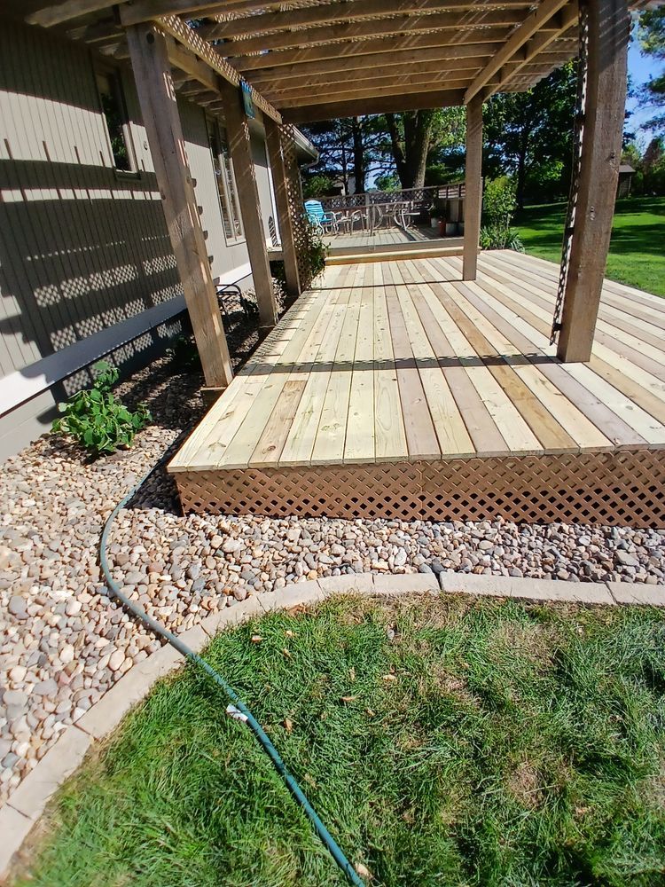 Wooden deck with a pergola, next to a house and grass.