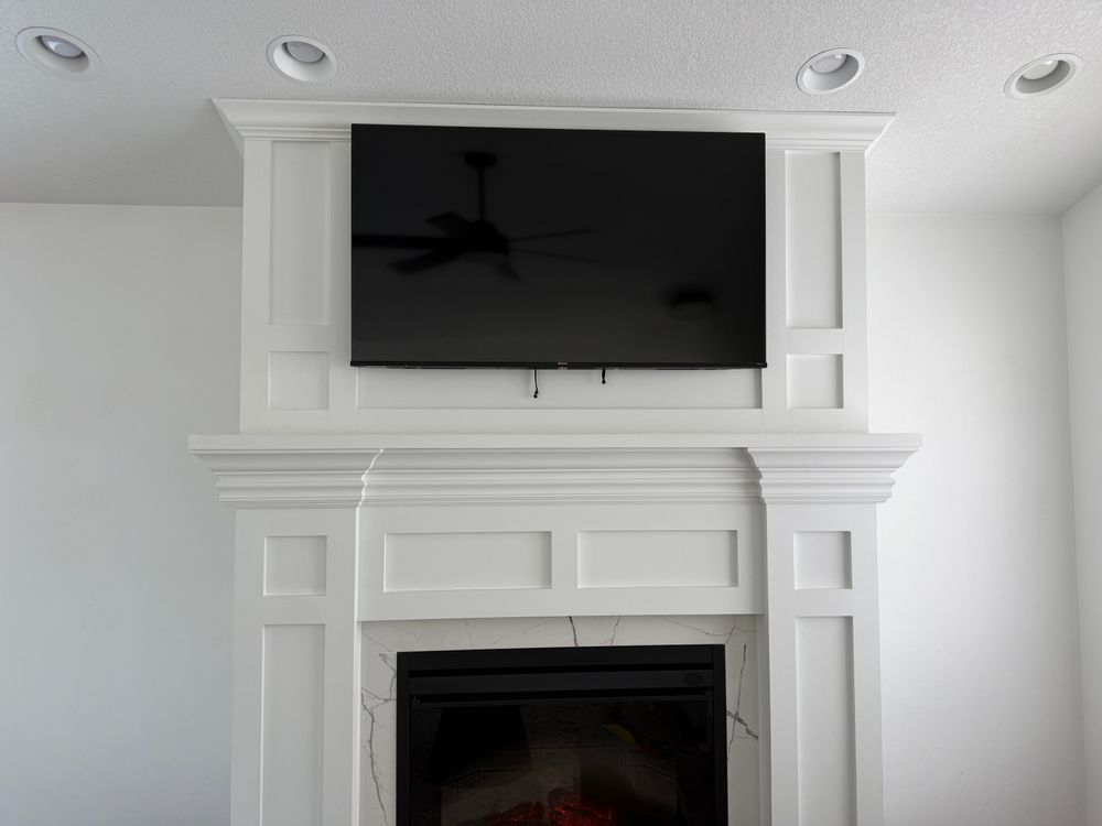 White fireplace with a black television mounted above, and recessed lighting.