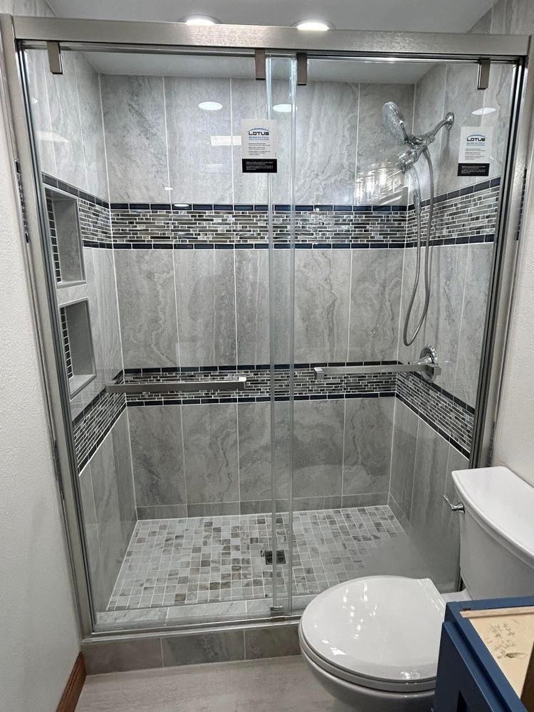 A gray-tiled shower with glass doors, mosaic floor, and a toilet to the right.
