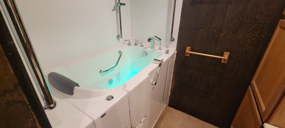 White walk-in bathtub with green illuminated water, chrome fixtures, and a brown wooden door.