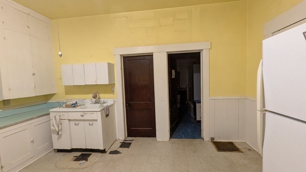 A kitchen with yellow walls, white cabinets, a dark door, and a refrigerator on the right.