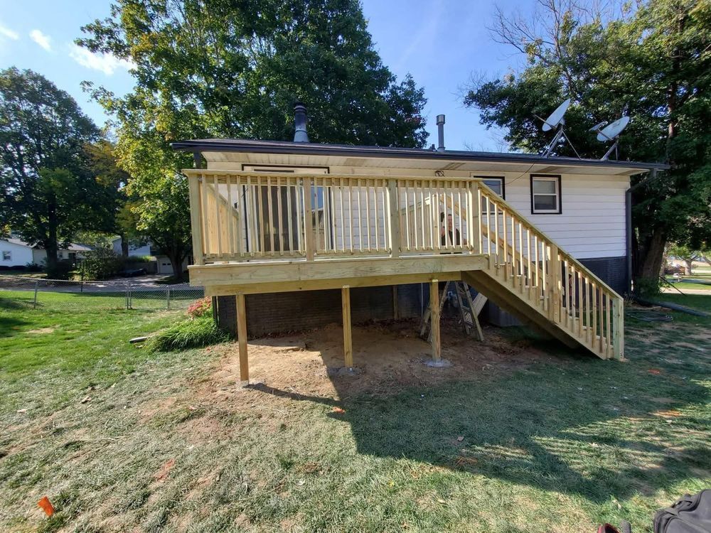 Wooden deck attached to a white house with stairs leading to the ground, on a grassy yard.
