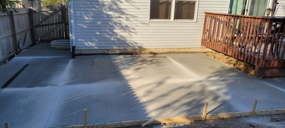 Newly poured concrete patio next to a house, deck, and fence.