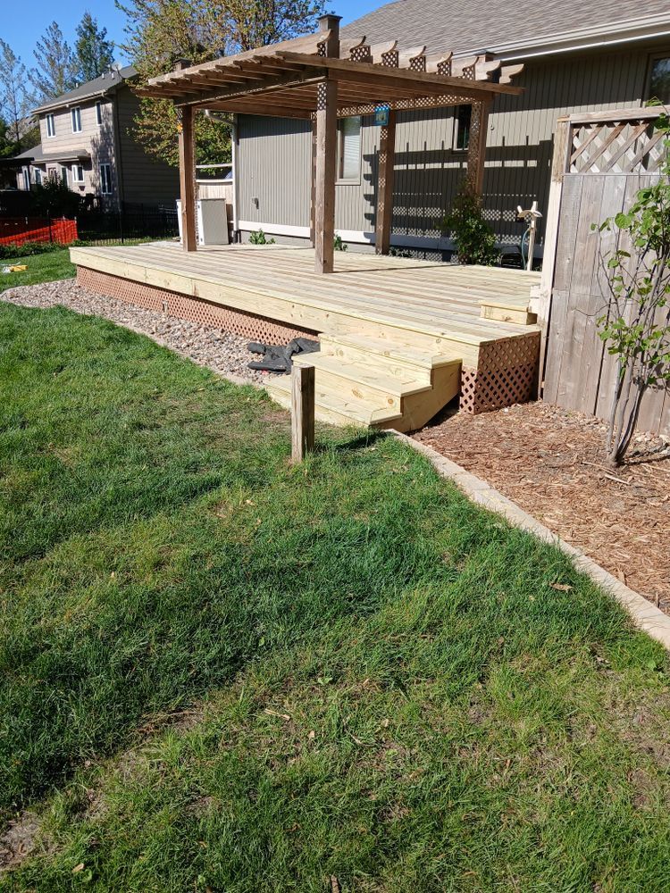 Wooden deck with pergola, steps, and gravel border in a grassy backyard.