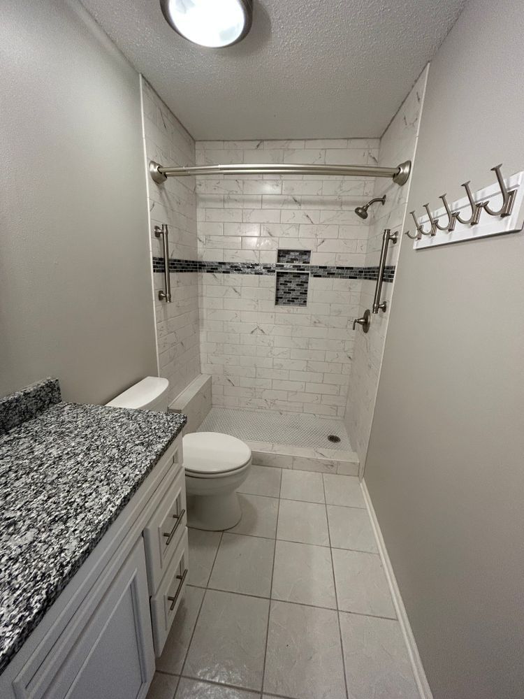 Bathroom with white and gray tile shower, vanity, toilet. Light gray walls, granite countertop.