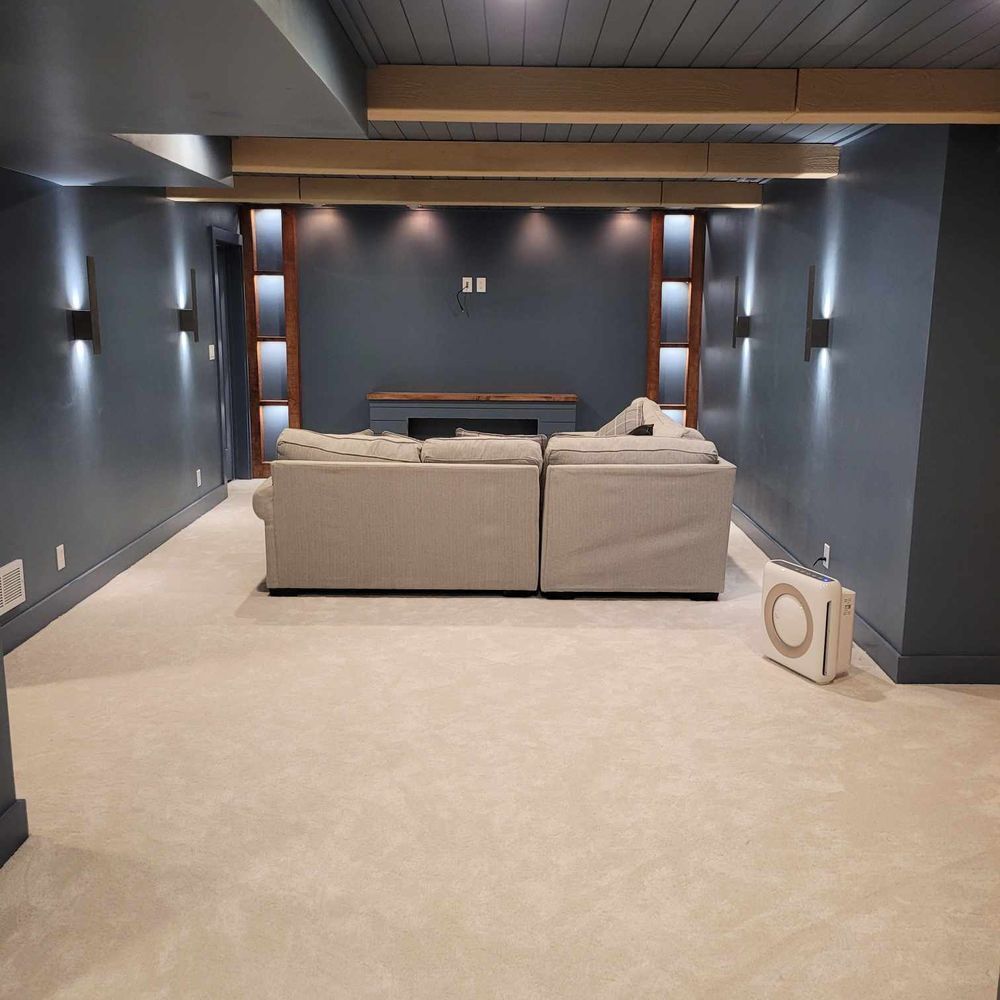 Cozy home theater with blue walls, light carpet, and a light-colored sectional sofa, lights and a ceiling feature.