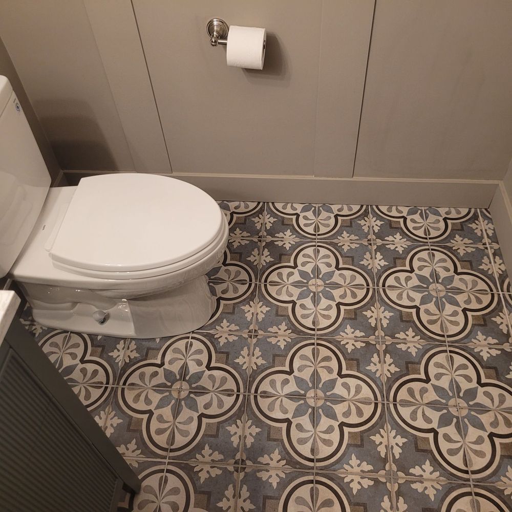 Toilet in a bathroom with patterned blue and gray floor tiles and a gray wall.