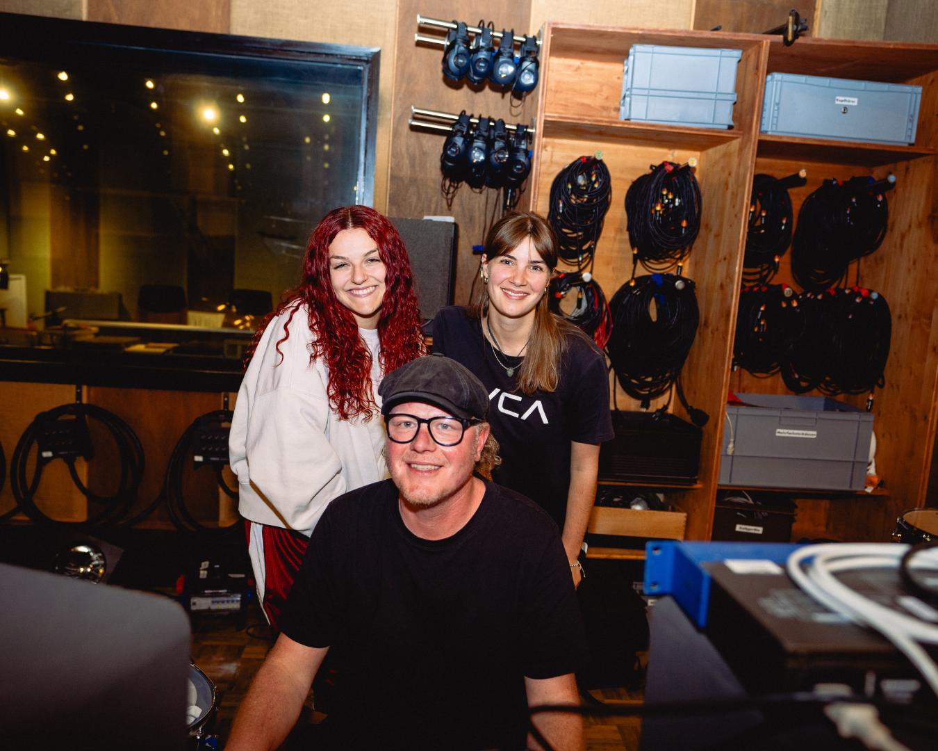 Drei Personen stehen in einem Ton-Studio und blicken in die Kamera.