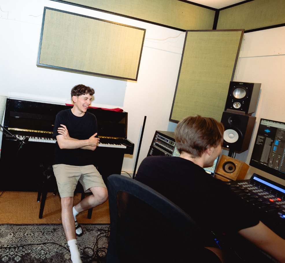 Ein Mann lehnt an einem Klavier in einem Aufnahme-Studio.