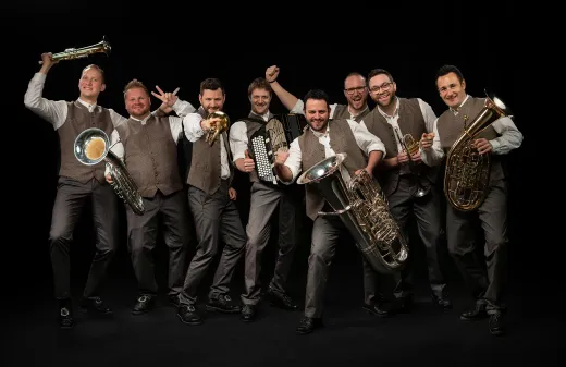 Eine Gruppe von Männern steht mit Blechblasinstrumenten in der Hand nebeneinander.