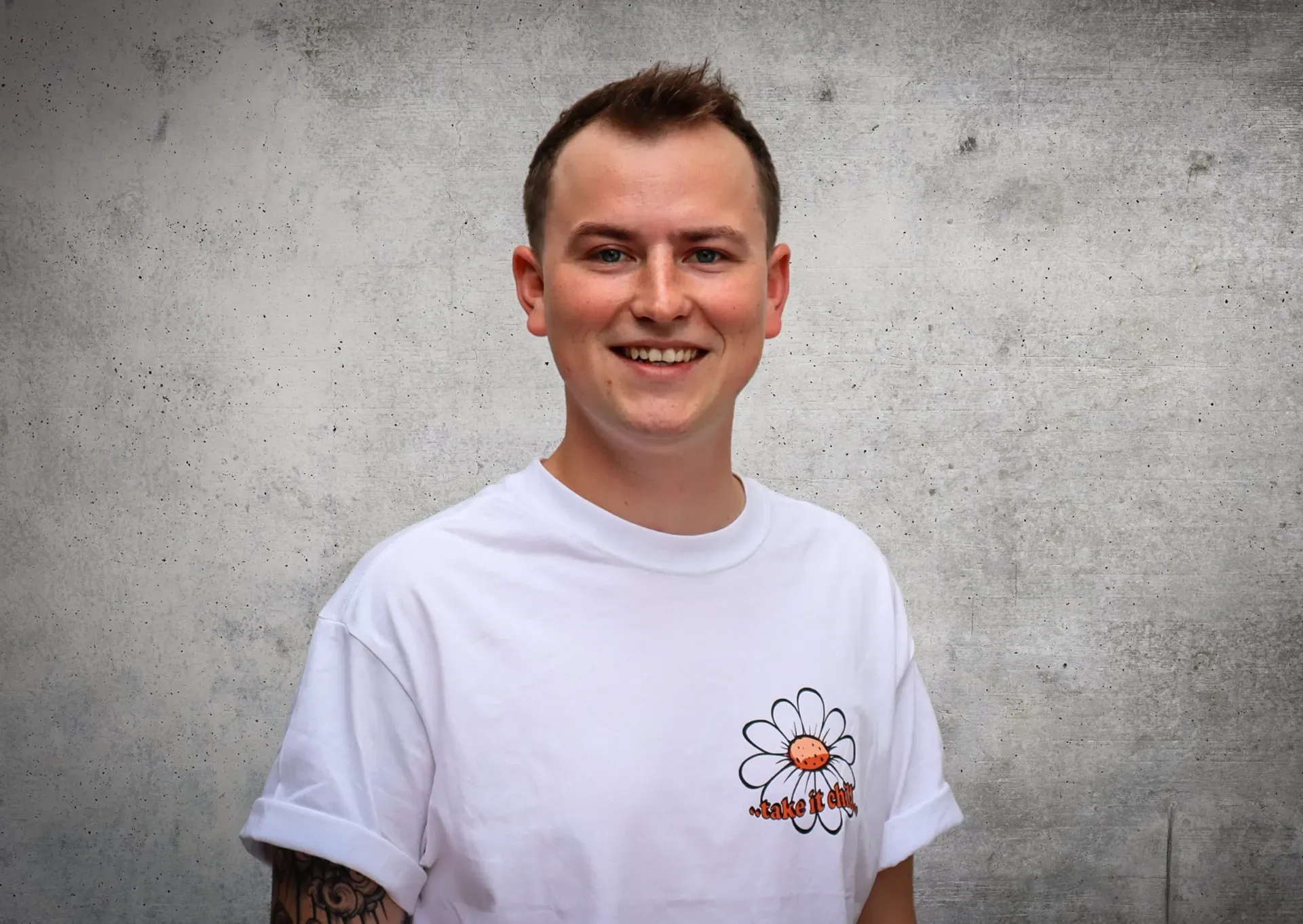 Ein Mann trägt ein weißes T-Shirt mit einer Blume darauf und lächelt.