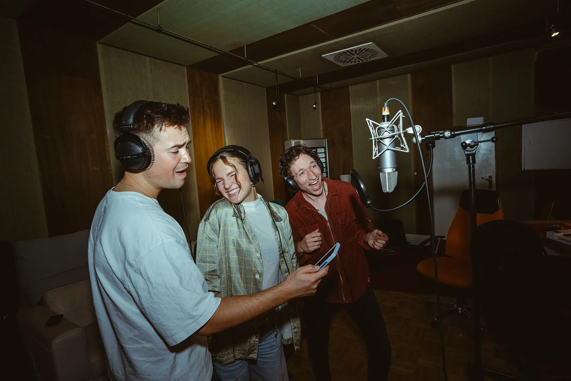 In einem Aufnahmestudio singt eine Gruppe von Menschen in Mikrofone.