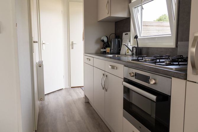 Smalle, moderne keuken met witte kasten, grijze werkbladen en een roestvrijstalen oven en kookplaat.