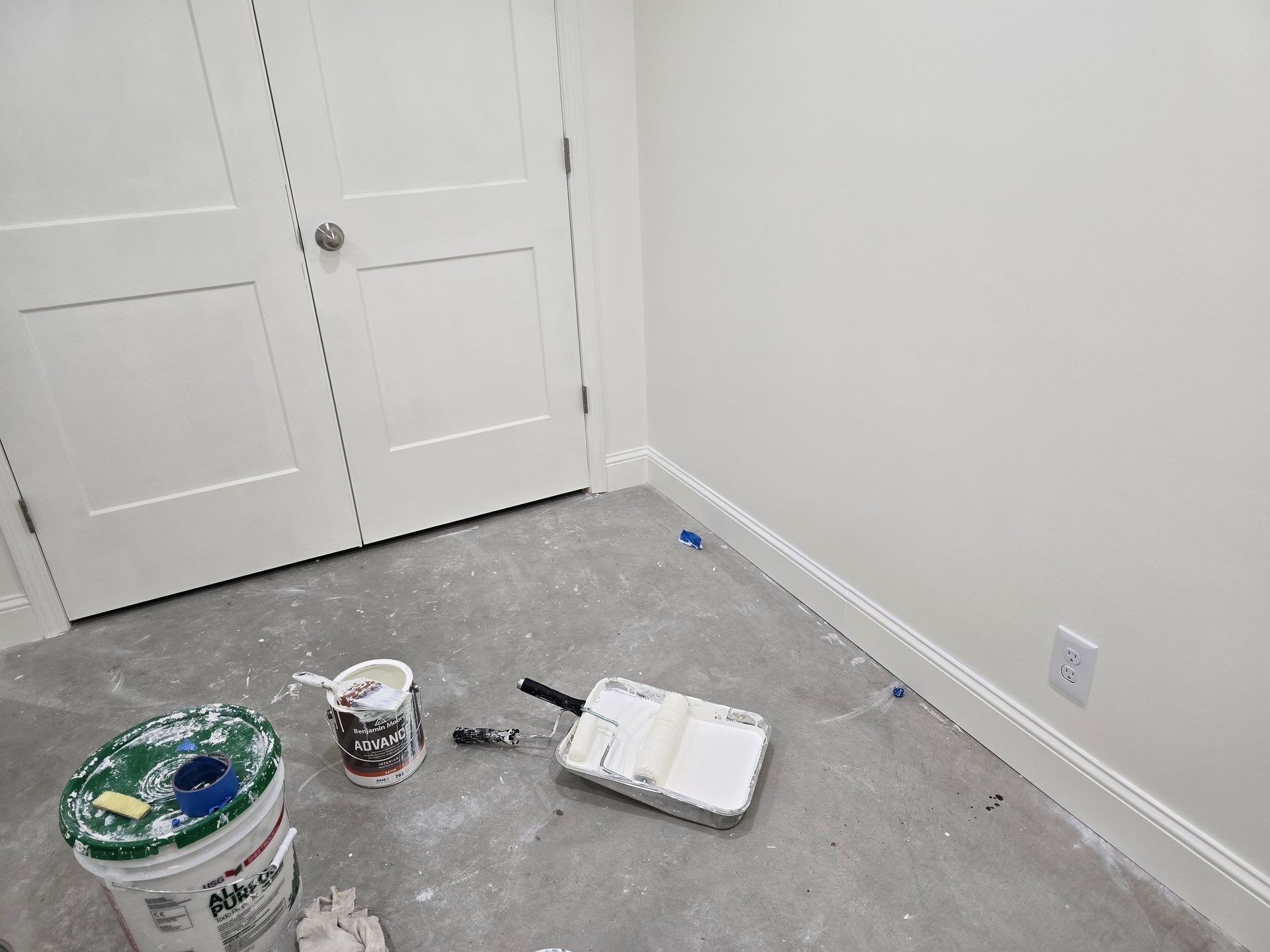 A room with buckets of paint and a paint roller on the floor.