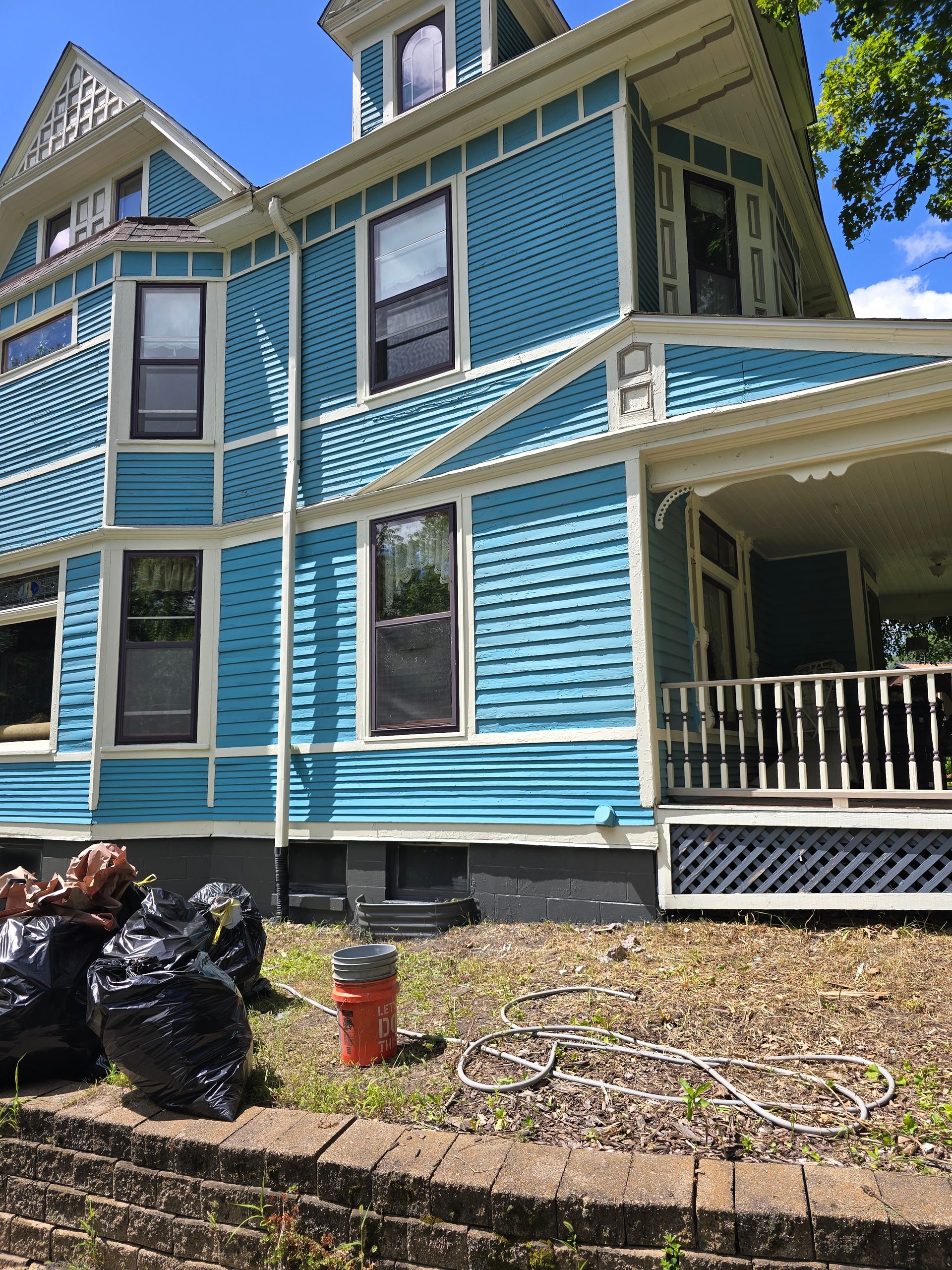 A blue and white house with a porch and trash bags in front of it
