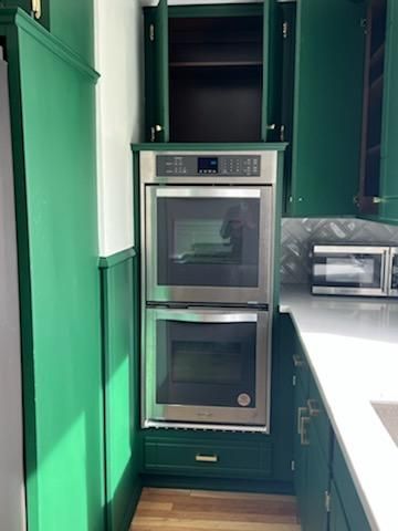 A kitchen with green cabinets and a double oven.
